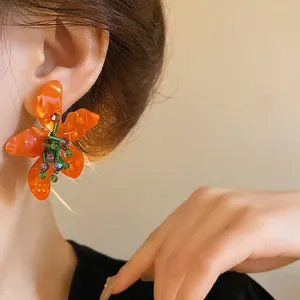 Close-up detail of orange floral acetate earrings with crystal accents on a model