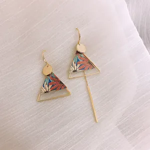 Close-up of ethnic asymmetric earrings with floral triangle design and gold tassel