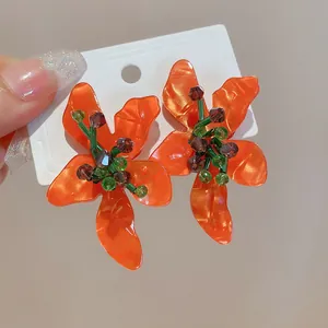 Close-up of vibrant orange flower earrings with detailed crystal stamen and green stems