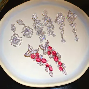 Detailed view of four pairs of sparkling zircon drop earrings on a cream ceramic plate.