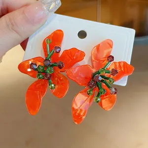 Close-up of bright orange flower earrings with green beads and purple crystals