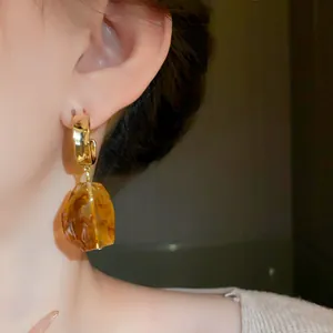 Close-up detail of retro Maillard style earrings with irregular amber resin drop and gold finish