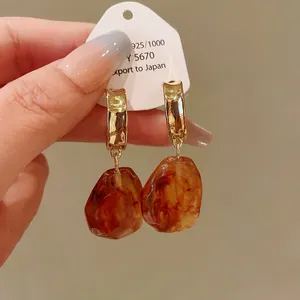 Detail of amber-colored irregular resin drop earrings with gold hoops.