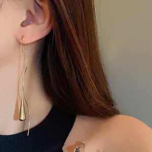 Close-up of elegant gold water drop tassel earrings with minimalist wavy line design