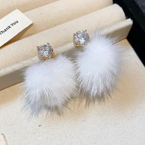 Detail view of zircon stud earrings with white faux fur pom-poms for winter