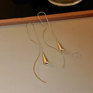 Macro view of gold water-drop threader earrings with elegant curved lines and polished finish