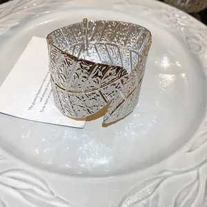 Macro detail of a minimalist silver leaf-textured cuff bracelet with gold accents.