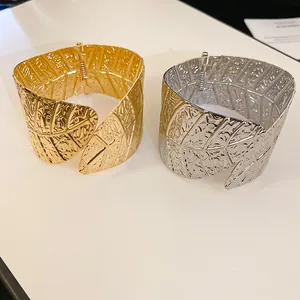 Macro view of gold and silver leaf-textured wide cuff bracelets on a white surface