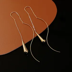 Detailed close-up of gold metal teardrop threader earrings with geometric curves