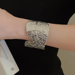Detailed close-up view of a minimalist silver wide cuff bracelet with a leaf pattern design