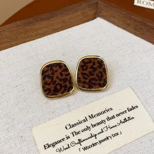 Dettaglio di orecchini a perno leopardati vintage con bordi dorati in una scatola di legno