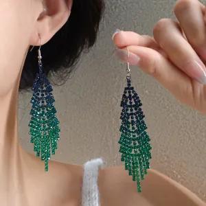 Close-up of blue-green rhinestone feather tassel earrings worn on ear.