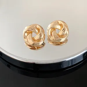 Close-up of elegant gold twisted knot stud earrings on a mirrored reflective surface