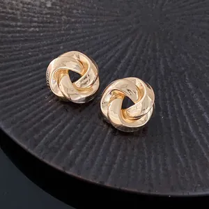 Close-up of elegant gold twisted knot stud earrings on a textured black surface
