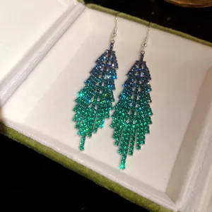 Detailed view of long feather-shaped drop earrings with gradient green rhinestones