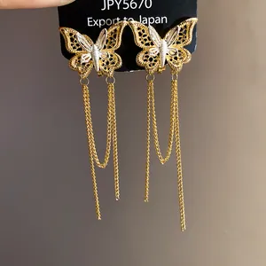 Dettaglio di orecchini a clip a farfalla placcati oro 18k con lunghe nappe a catena.