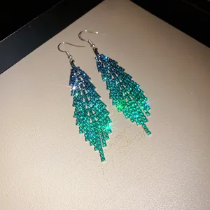 Macro detail of long feather tassel earrings with blue to green gradient rhinestones