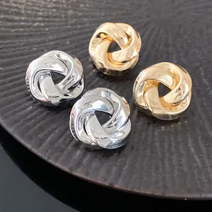Detail view of silver and gold twisted knot metal stud earrings with polished finish