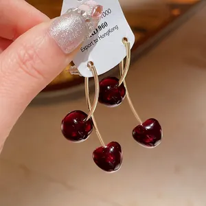 Close-up detail of glossy dark red cherry resin earrings with gold stems