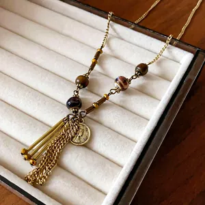 Close-up detail of vintage ceramic beads and metal coin pendant on long tassel necklace