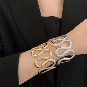 Nahaufnahme von gewellten Metallmanschetten in Gold und Silber auf einem schwarzen Blazer.