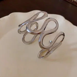 Makrodetail eines abstrakten gewellten silbernen Metall-Armreifs auf einem Keramikteller