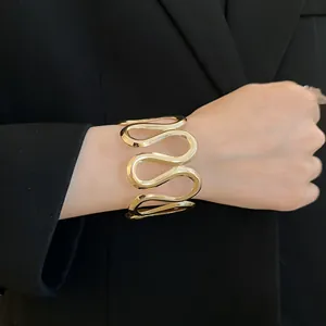 Detailansicht eines goldfarbenen, wellenförmigen Armreifs an einem Handgelenk