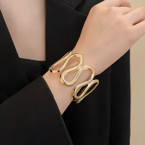 Detailansicht eines goldfarbenen, wellenförmigen Metallarmreifs über einem schwarzen Blazer.
