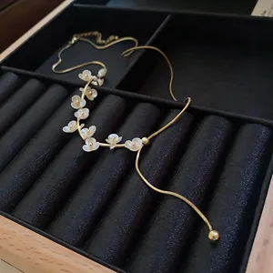 Vue détaillée d'un collier floral doré avec des perles dans un écrin noir élégant.