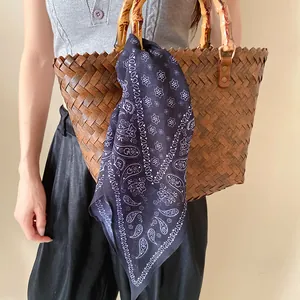 Gros plan du foulard en soie à motif paisley noué sur un sac tressé
