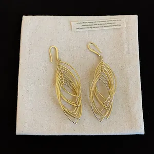 Close-up detail of gold oval pleated layered dangle hook earrings on fabric