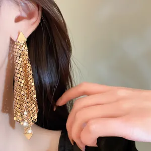 Close-up of gold triangle sequin irregular tassel earrings worn on a model's ear
