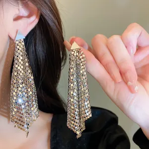 Close-up of irregular silver sequin earrings with triangle studs shown on an ear.