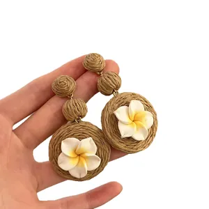 Orecchini artigianali in rafia con fiori in argilla su un semplice sfondo bianco