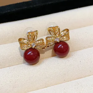 Detail view of 18k gold plated stud earrings with clear zircon and deep red pearl
