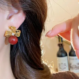 Close-up detail of 18K gold-plated flower stud earring with red pearl and zircon on model ear