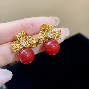 Detail view of exquisite 18k gold plated bow earrings with zircon and red pearls