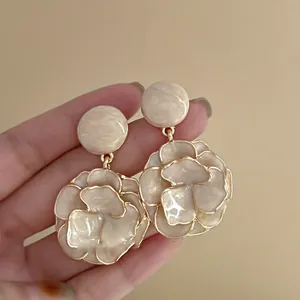 Detail view of retro flower drop earrings with a creamy enamel finish and gold edges