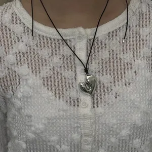 Close-up of a silver organic heart pendant necklace with a black cord on a model.