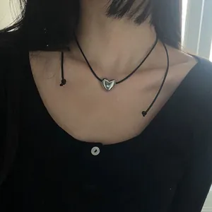 Close-up of a minimalist polished silver heart pendant necklace on a thin black cord.