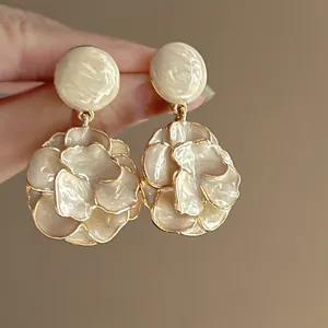 Close-up detail of vintage creamy floral enamel drop earrings with gold-plated edges