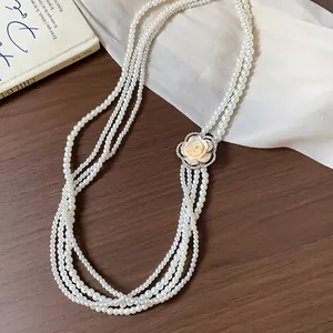 Macro shot of multi-strand pearl necklace featuring a rhinestone-embellished rose flower.