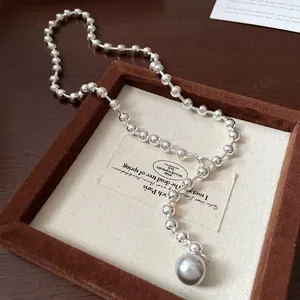 Primer plano de un collar de cuentas plateadas con colgante de perla gris en bandeja.