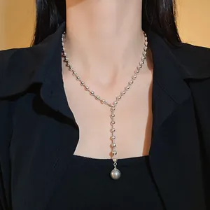 Primer plano de un collar de perlas sintéticas minimalista en Y en el cuello del modelo.