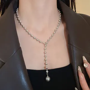 Detalle de un collar minimalista en Y con cuentas plateadas y una perla gris