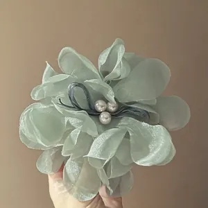 Macro view of a light green organza flower hair clip with elegant pearl center detail