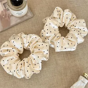 Close-up of elegant cream satin scrunchies featuring classic black polka dot patterns