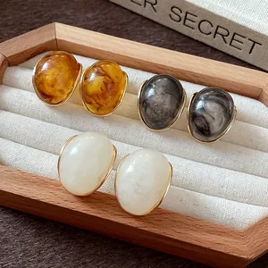 Primer plano de pendientes retro de resina con texturas de mármol y ámbar en bandeja de madera.