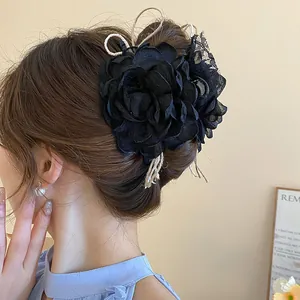 Close-up of large 3D black fabric flower hair claw clip worn in a messy bun hairstyle