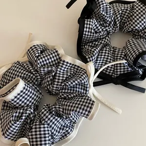 Close-up view of two black and white gingham hair scrunchies with decorative ribbons